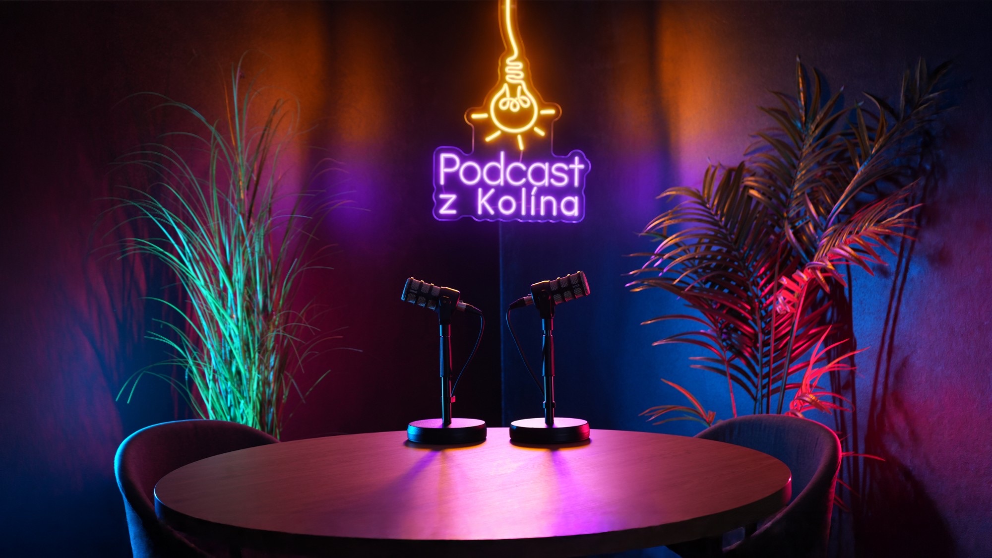 Podcastové studio A s neonovým logem Podcast z Kolína a dvěma mikrofony na kulatém stole
