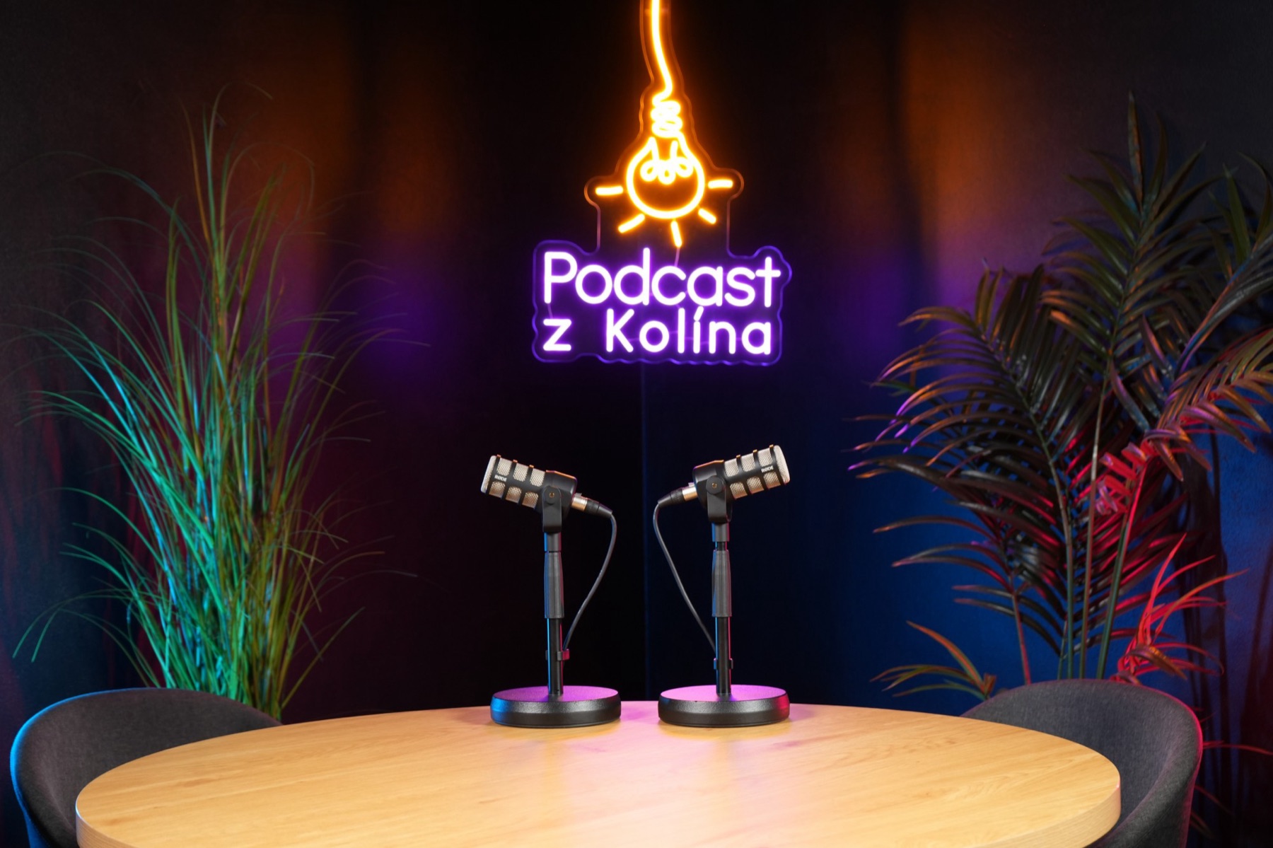 Studio A: tmavé studio s neonovým logem, kulatým stolem a dvěma mikrofony